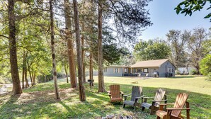 Una casa con patio, tres sillas Adirondack y un pozo de fuego.