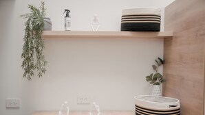 A minimalist room with a wooden floor, a white wall, a shelf with a plant, a white vase, and two white sculptures.