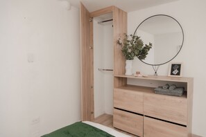 Un dormitorio con cama, un armario de madera, un espejo y un pequeño estante con adornos.