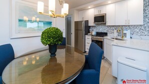A modern kitchen with white cabinets, stainless steel appliances, and a glass dining table with blue chairs.