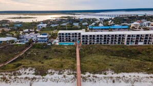 An aerial view of a coastal area with a long wooden boardwalk leading to a building with multiple balconies.