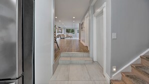 A modern kitchen with a stainless steel refrigerator, a wooden staircase leading to a living area, and a view of the outdoors. - Casa Mattia 4BR Luxury Mountain Home (Suffern)
