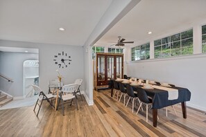 A dining area with a long table set for six, white chairs, and a clock on the wall. - Casa Mattia 4BR Luxury Mountain Home (Suffern)