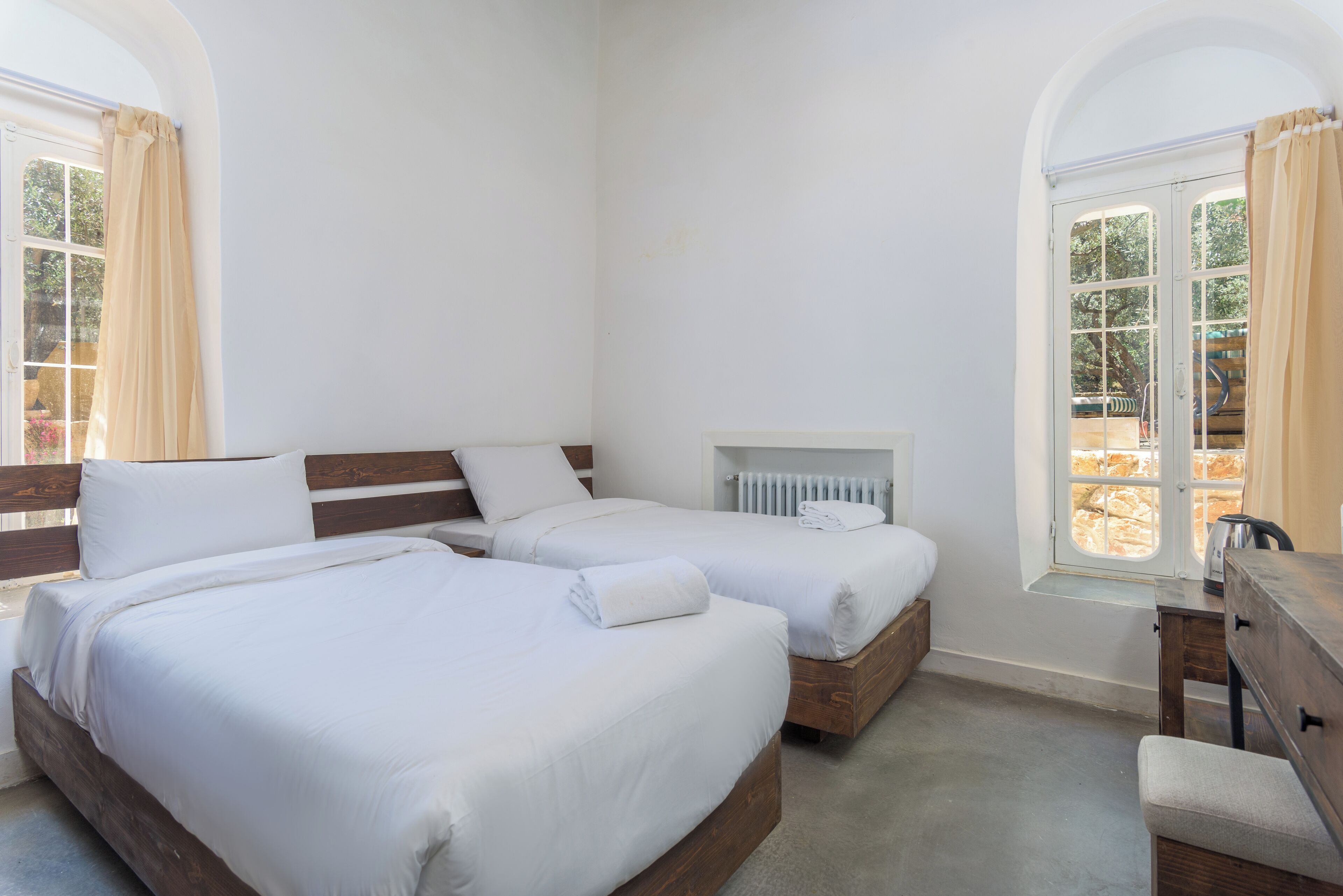 A room with two beds, a wooden dresser, a radiator, and a window with curtains.