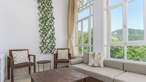 Un salon chaleureux avec une table basse en bois, deux fauteuils, un canapé avec des coussins, une petite table ronde et une plante fixée au mur.