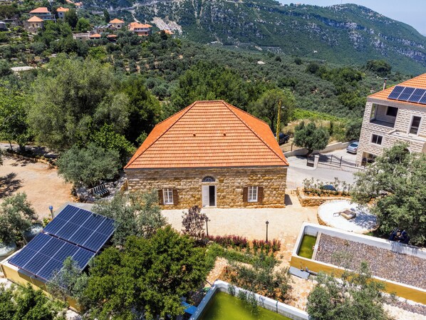 A stone building with a red-tiled roof, surrounded by greenery and a mountainous backdrop. - LAuberge de Douma Full House in Batroun (Douma)