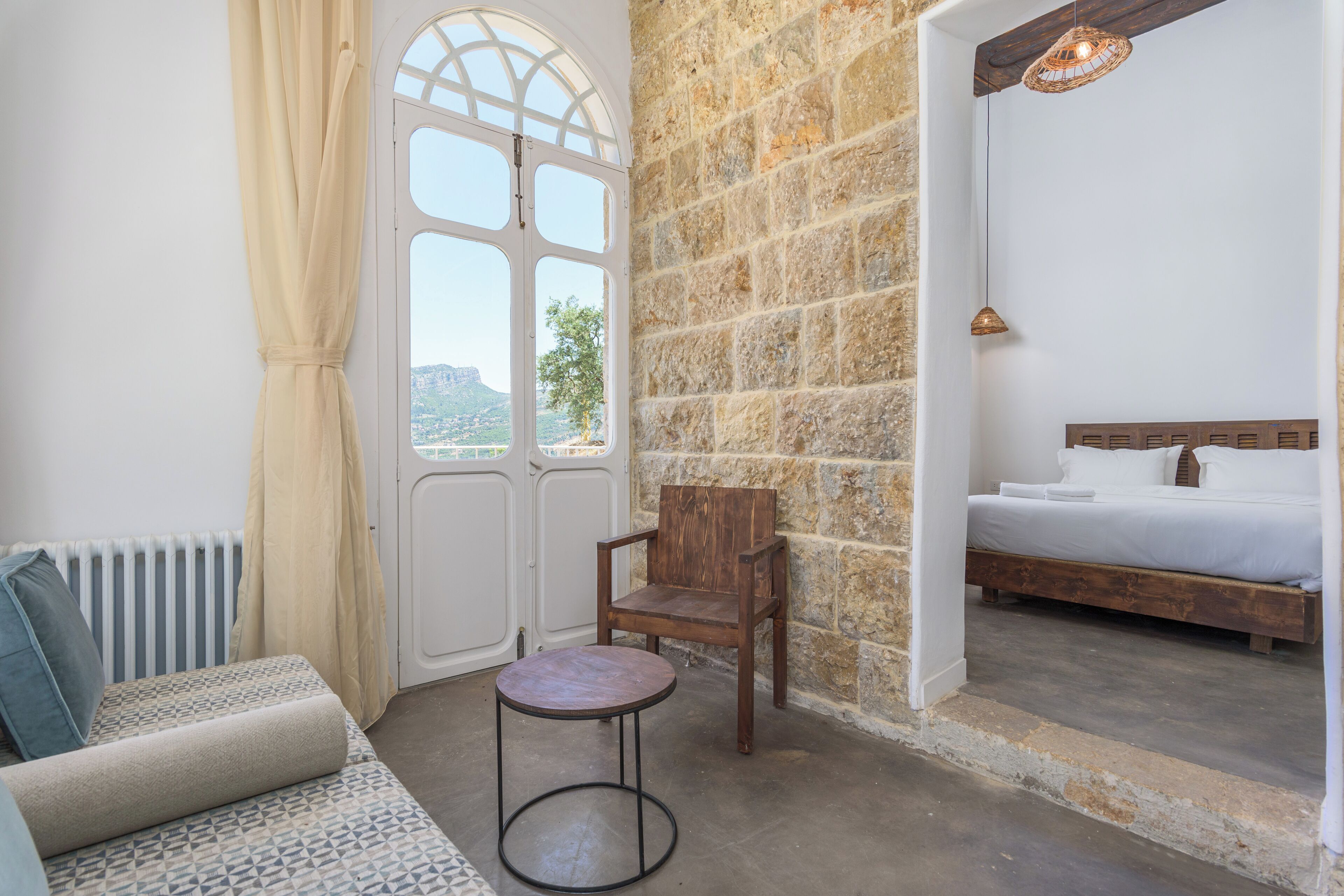 A bedroom with a stone wall, a bed, a wooden chair, and a small table.