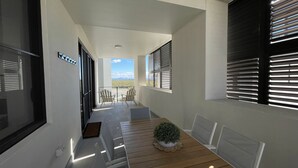 Un couloir étroit doté d’un plancher en bois, une petite table sur laquelle est posée une plante en pot, et deux chaises.