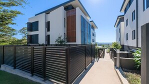 Un immeuble résidentiel moderne doté d’une entrée sécurisée, d’un chemin menant à l’entrée et offrant une vue sur le paysage environnant.