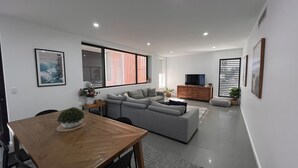 Un salon moderne avec un canapé gris, une table à manger en bois et un téléviseur posé sur un meuble en bois.