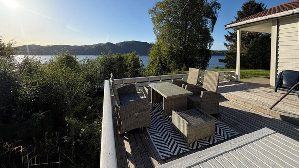 Eine Holzterrasse mit Korbmöbeln, mit Blick auf einen See und Hügel.