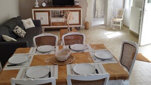 A dining area with a wooden table set for four, surrounded by wicker chairs. A television is mounted on a cabinet above the table. - 2 minutes from Beauval Zoo - SEIGY - LE GITE DES ECUREUILS 4 / 6 persons (Seigy)