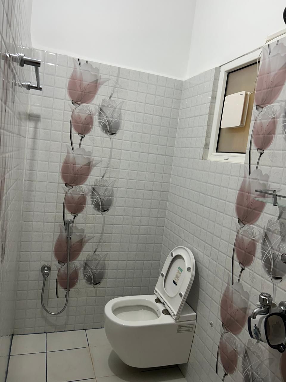 Ein Badezimmer mit Toilette, einer Duschkabine mit Glastür und einem kleinen Fenster über der Toilette.