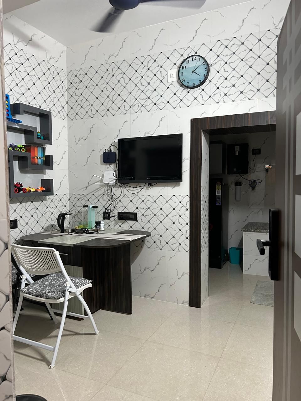 A modern kitchen with a marble backsplash, a built-in TV, and a dining area with a chair.