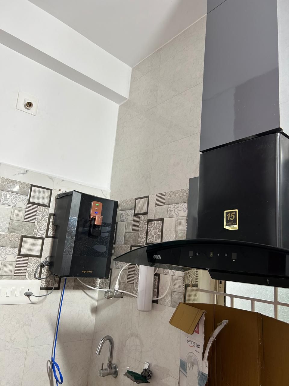 A kitchen with a black range hood, a water heater, and a tiled backsplash.