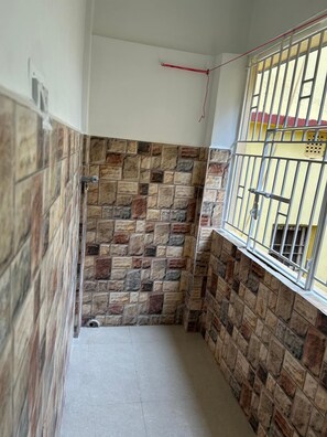 A narrow hallway with stone-patterned walls, a metal railing on the right, and a window with bars.