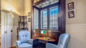 A room with two blue armchairs, a wooden side table, a floor lamp, and a window with stained glass. - Roman Holiday Republic (Roma)