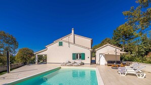 Une maison à deux étages dotée d’une piscine, d’un espace salon extérieur et d’une terrasse couverte.