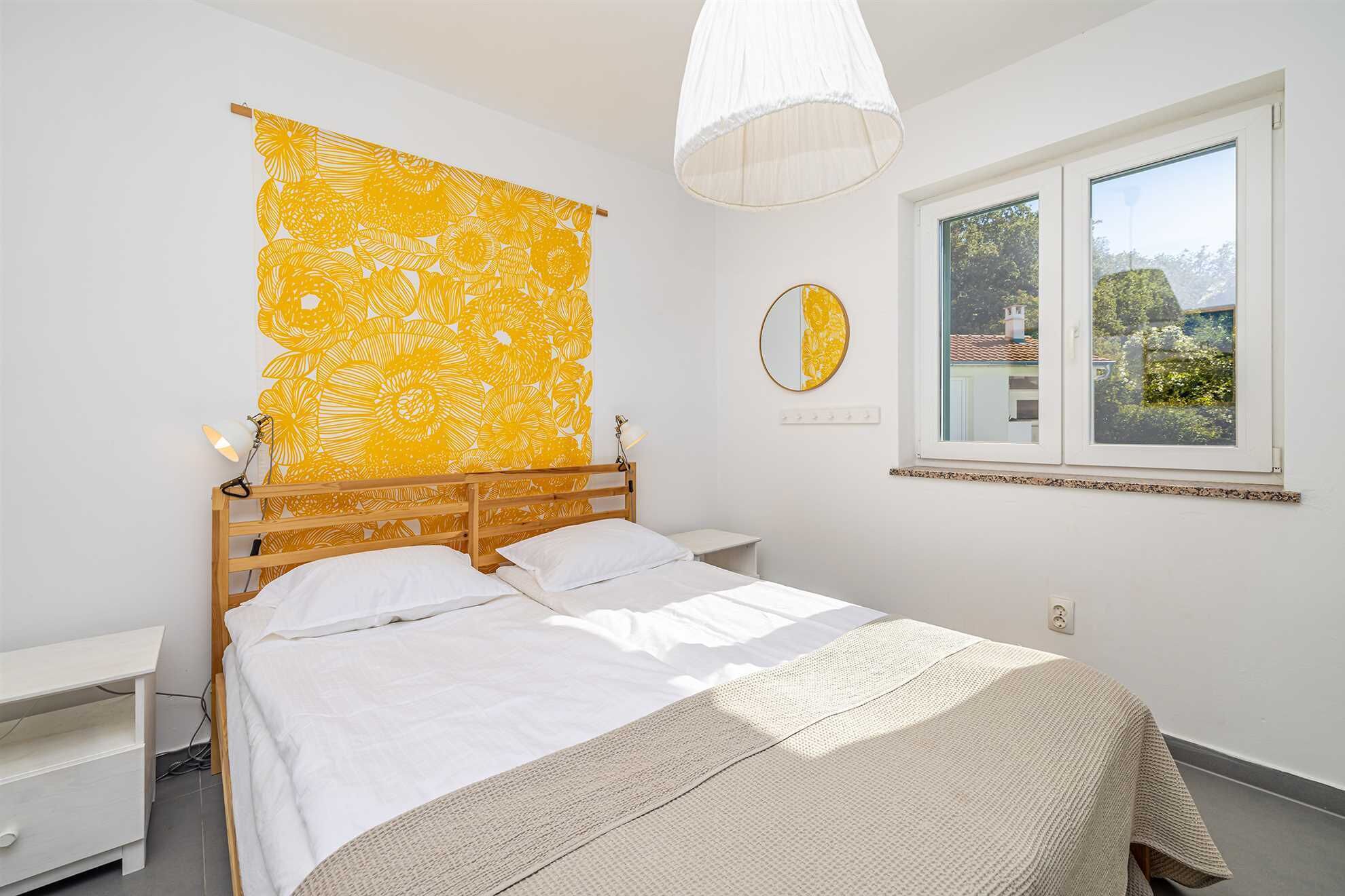 A bedroom with a bed, bedside tables, a window with a view, a hanging light fixture, and a wall with a floral pattern.