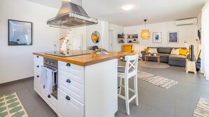Une cuisine moderne avec un îlot central, un coin repas avec un canapé et un salon avec un divan et un téléviseur.
