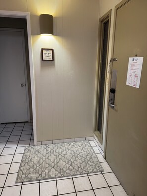 A hotel entrance with a tiled floor, a wall-mounted light, a door with a sign, and a floor plan on the wall. - Ocean View, Fully AC'd, 1 Bed/Ba, Full Kitchen (Kapaa)