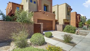 A modern multi-story residential building with a brick facade, a gated entrance, and a well-maintained garden with various shrubs and plants. - Dog Friendly Tucson 3bd 2.5ba Family Home Snowbirds Pool Access Fire Pit Grill (Tucson)
