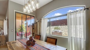 A dining area with a wooden table, chairs, and a rug. There is a window with a view of a desert landscape. - Dog Friendly Tucson 3bd 2.5ba Family Home Snowbirds Pool Access Fire Pit Grill (Tucson)