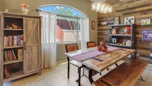 A dining area with a wooden table, chairs, a bookshelf, and a window with curtains. - Dog Friendly Tucson 3bd 2.5ba Family Home Snowbirds Pool Access Fire Pit Grill (Tucson)
