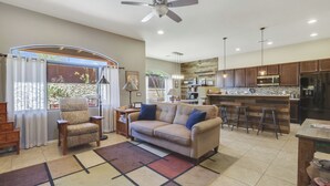 A spacious living area with a sofa, armchairs, and a coffee table. A kitchen with a bar and stools is visible in the background. - Dog Friendly Tucson 3bd 2.5ba Family Home Snowbirds Pool Access Fire Pit Grill (Tucson)