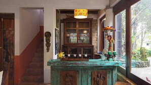 A rustic interior with a staircase, a wooden cabinet with glass doors, and a window with a view of greenery.
