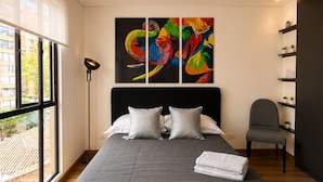 Ein modernes Schlafzimmer mit einem großen Bett, einer Stehlampe, einem Sessel und Blick ins Freie.