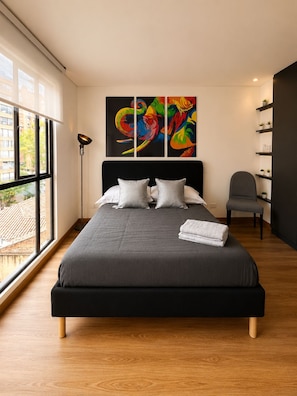 Een moderne slaapkamer met een groot bed, een vloerlamp, een stoel en uitzicht op het omliggende landschap.