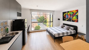 Ein modernes Schlafzimmer mit einem Bett, einem kleinen Tisch und Blick auf die Stadt durch große Fenster.