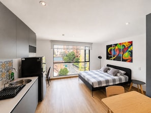 Een moderne slaapkamer met een bed, een klein tafeltje en een stadszicht door grote ramen.