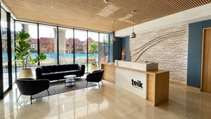 Ein moderner Empfangsbereich mit Holzboden, einer Rezeption, einem schwarzen Sofa und einem großen Fenster mit Blick auf Gebäude.