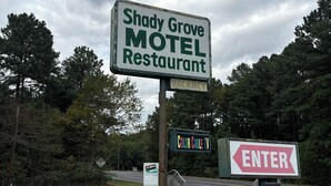 Une enseigne de motel avec l’inscription « Chambres disponibles », un panneau indiquant la direction du « Restaurant du Shady Grove Motel », et une autre enseigne avec l’inscription « Entrée » le long de la route.