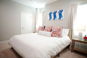 A bedroom with a large bed, a nightstand, a wall art piece, and a window with curtains. - The Lily Loop Retreat (Oxford)
