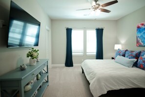 Une chambre à coucher avec un lit, un téléviseur fixé au mur, un ventilateur de plafond et une fenêtre avec des rideaux.