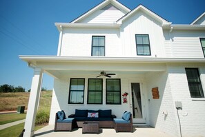 A two-story white house with a covered porch, a ceiling fan, and a large window with shutters. - The Lily Loop Retreat (Oxford)