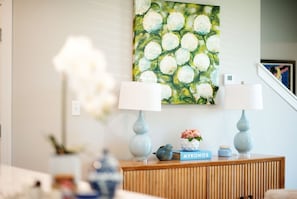 Ein Zimmer mit einem Holztischchen, zwei Lampen, einem Gemälde und einer Vase mit Blumen.