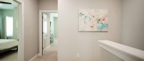 Un couloir doté d’un sol recouvert de moquette, une porte donnant sur une chambre à coucher et un tableau abstrait accroché au mur.
