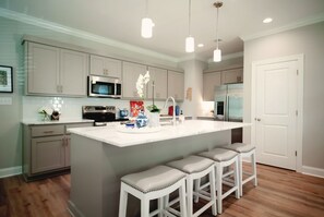 A modern kitchen with a central island, bar stools, a microwave, a stove, and a refrigerator. - The Lily Loop Retreat (Oxford)