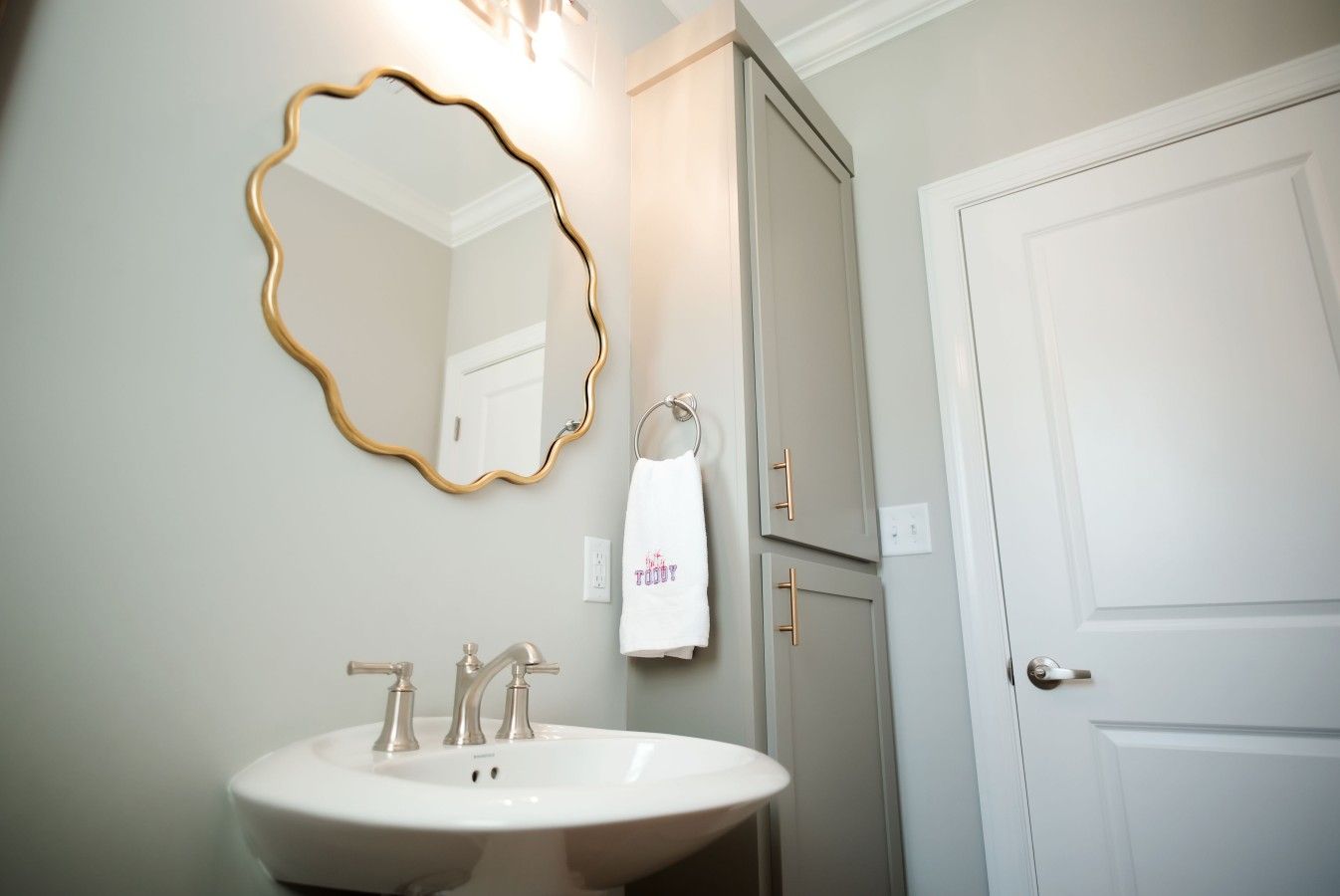 A bathroom with a white sink, a gold-framed mirror, and a white towel hanging on a towel rack.