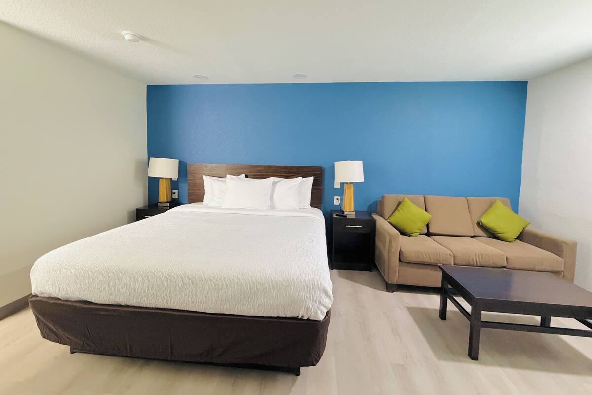 A hotel room with a large bed, a sofa, a coffee table, and two bedside tables with lamps.