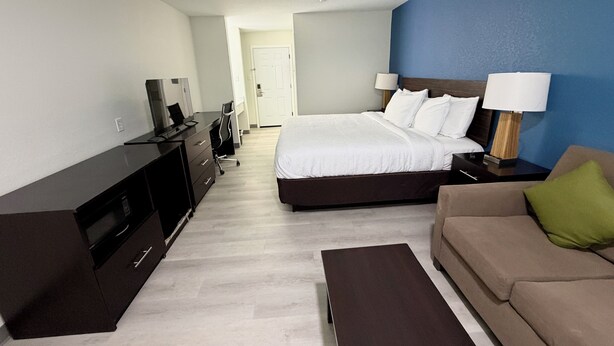 A hotel room with a bed, a desk, a TV, a sofa, and a lamp.
