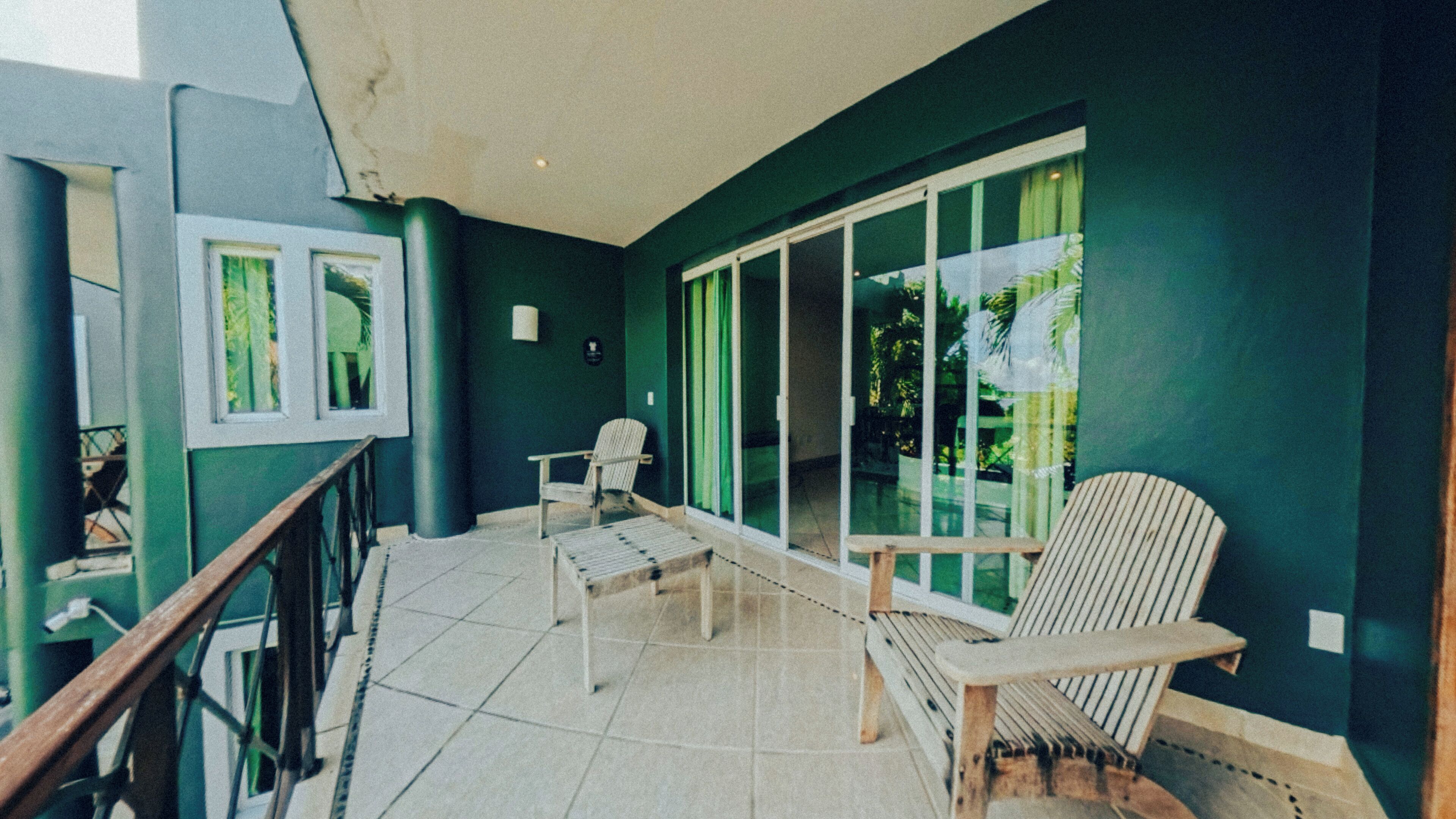 Un balcon avec une chaise, une table et une vue sur la verdure, visible à travers des portes vitrées.
