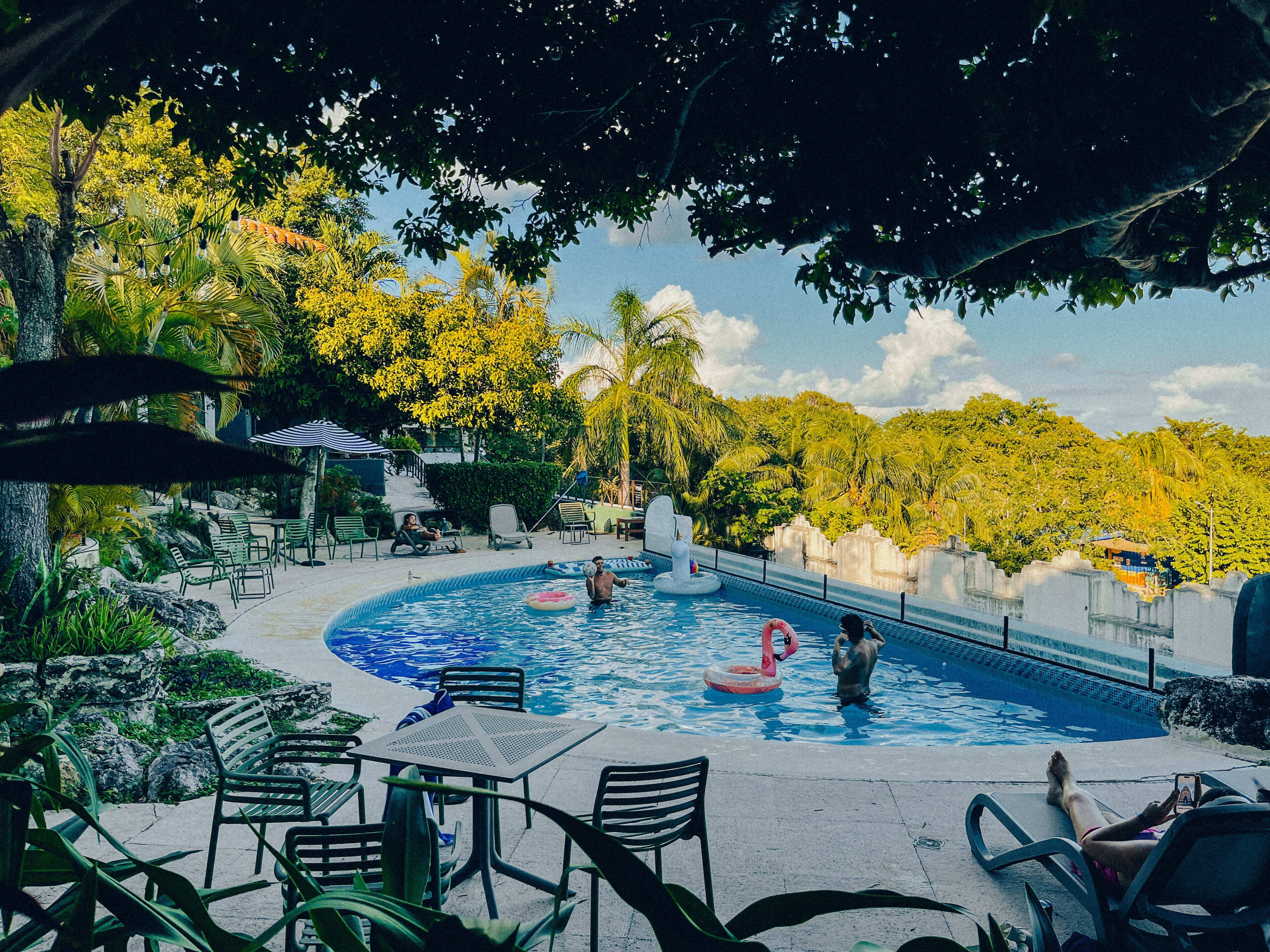 A pool area with lounge chairs and a table, surrounded by tropical vegetation and a view of the sky.