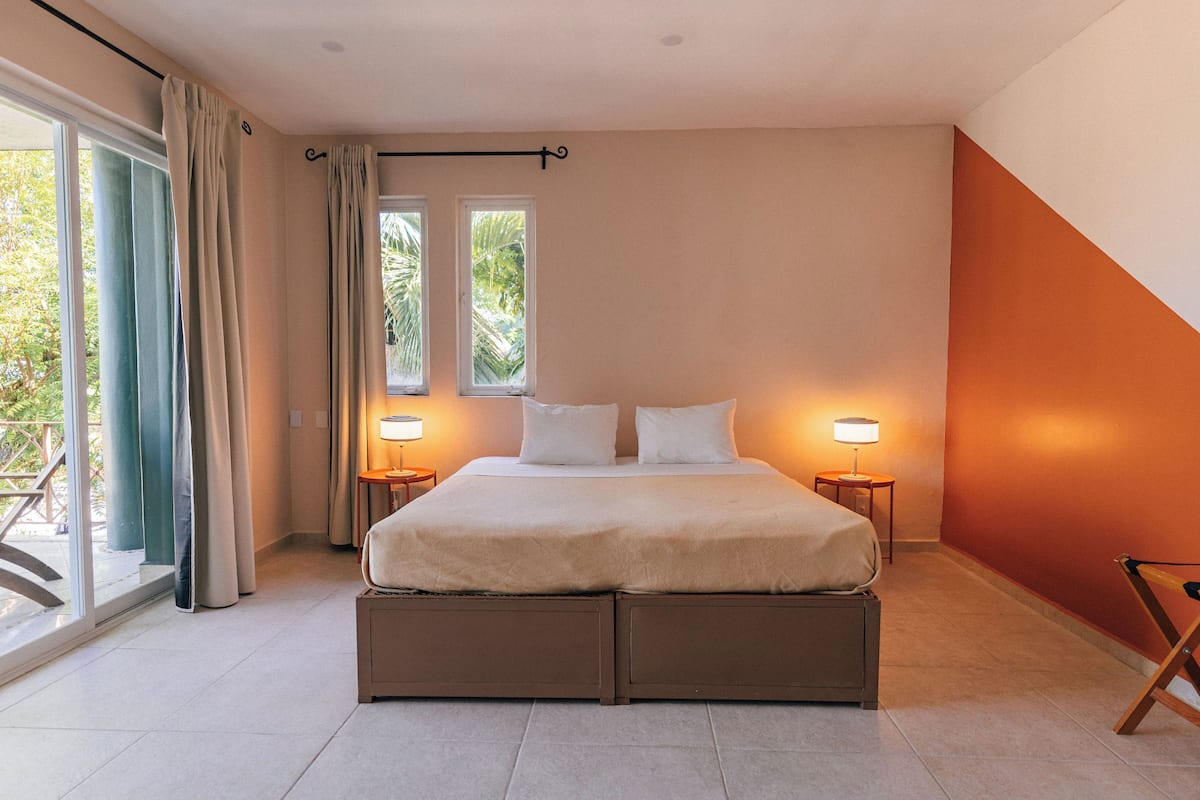Een slaapkamer met een groot bed, twee bedlampen, uitzicht op de omgeving via een schuifdeur, en een raam met gordijnen.