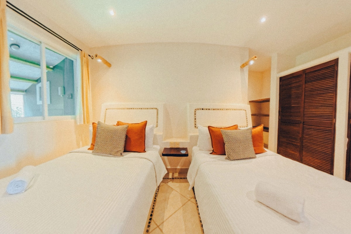 Een hotelkamer met twee bedden, een kleine tafel en een raam met gordijnen.
