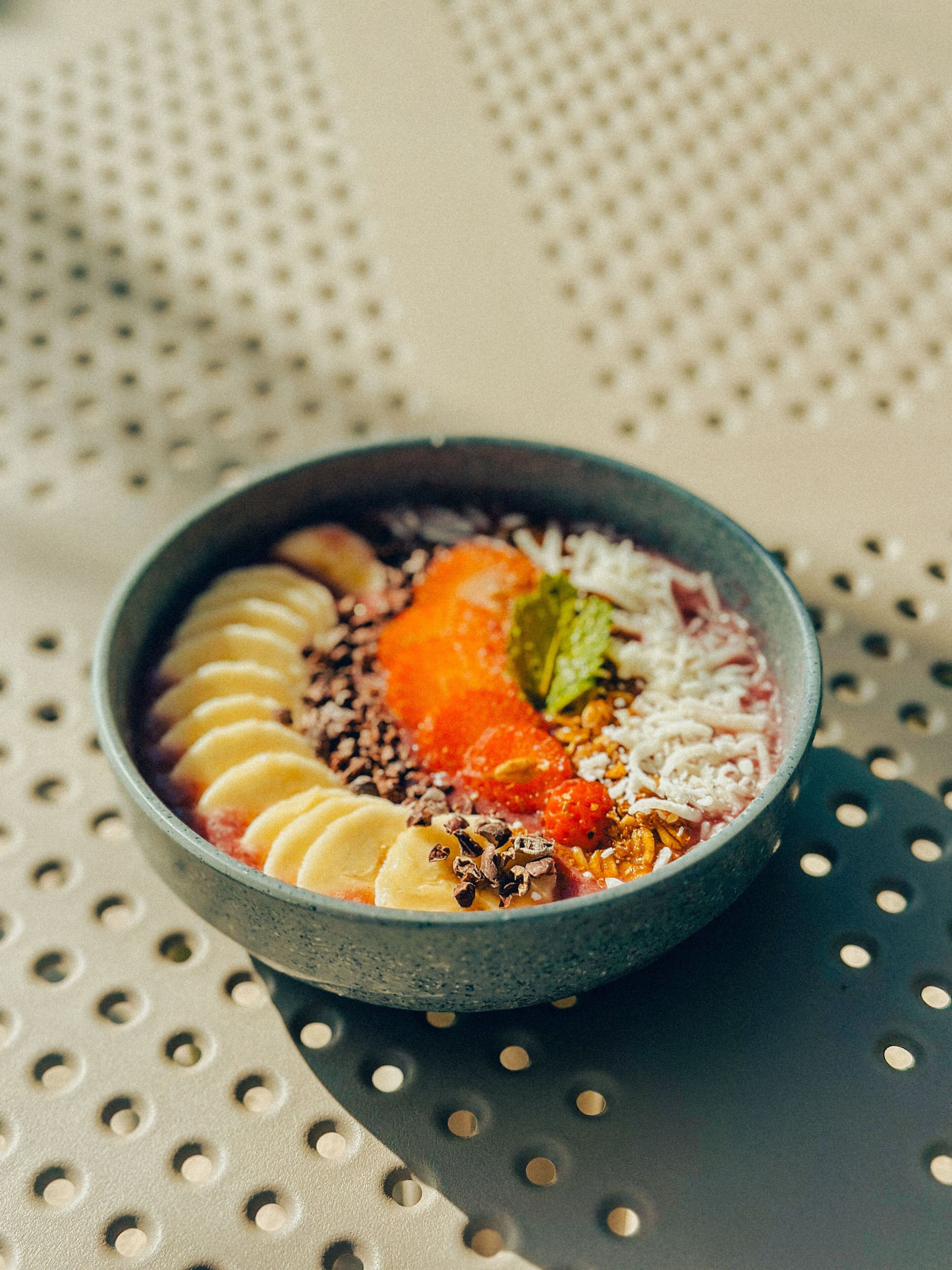 A bowl of food with various toppings on a perforated surface.